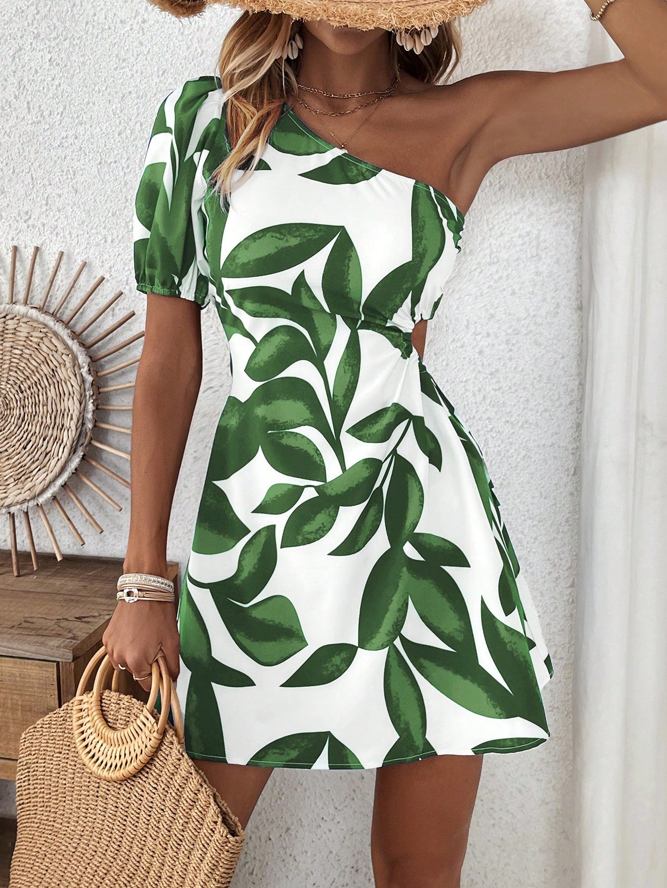 Asymmetrical short mini on white background with two toned green leaf print. one arm is bare and the other arm has a short sleave on it. Model is facing forward